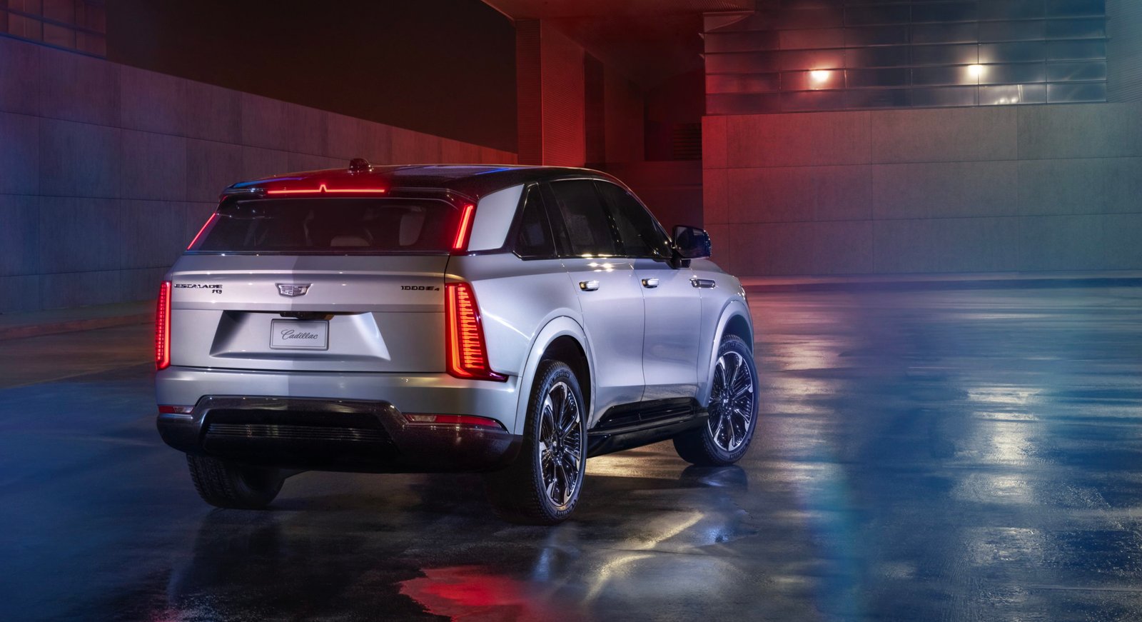 Rear 7/8 view of Cadillac ESCALADE IQ Sport in Flare Metallic at night.